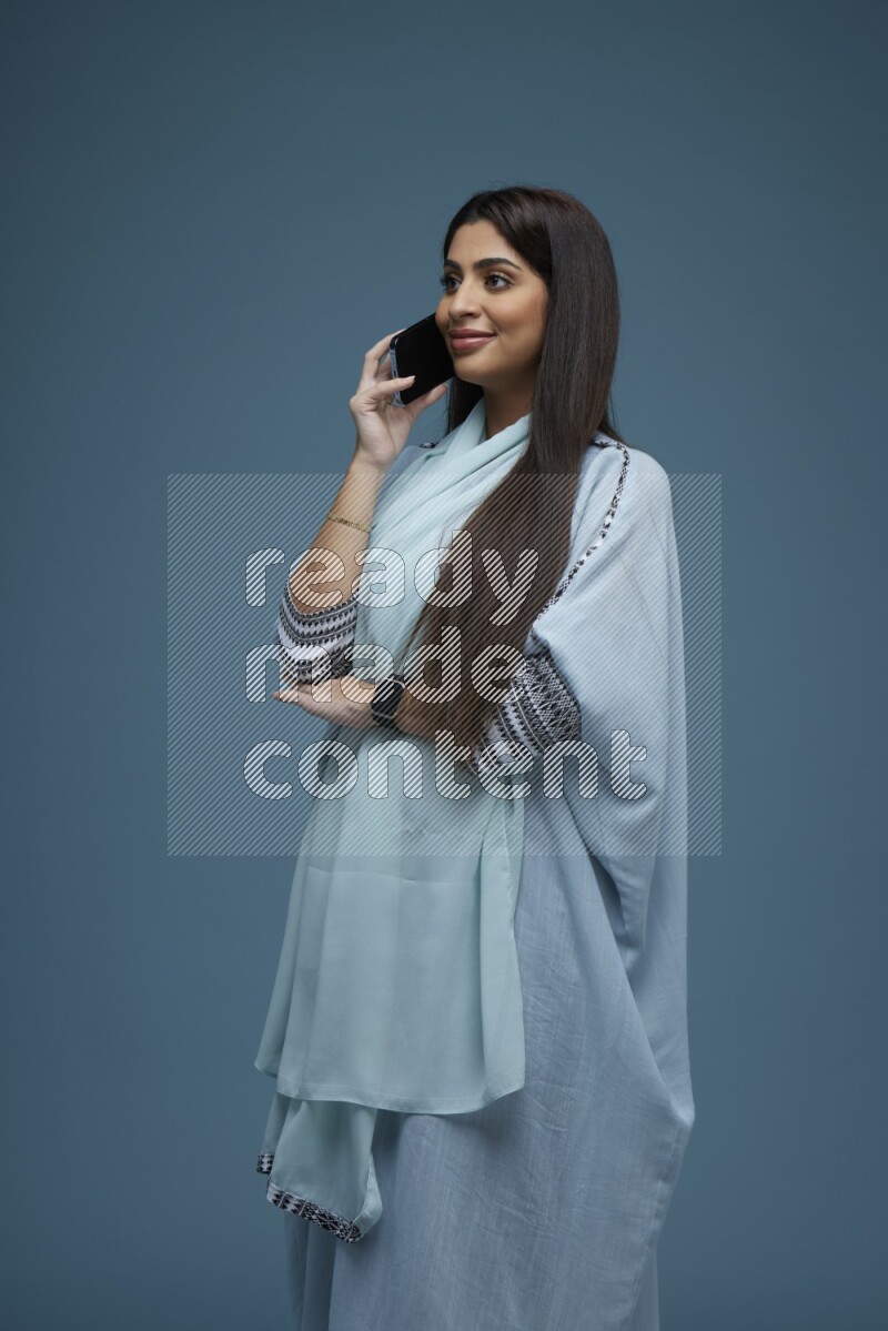 A Saudi woman having a Call in a blue background wearing a blue Abaya with no hijab
