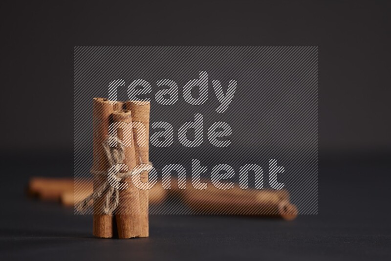 4 Cinnamon sticks stacked and bounded with more sticks in the background on black flooring