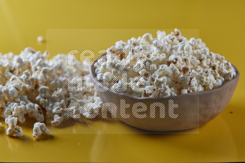 A brown pottery bowl full of popcorn with popcorn beside it on a yellow background in different angles