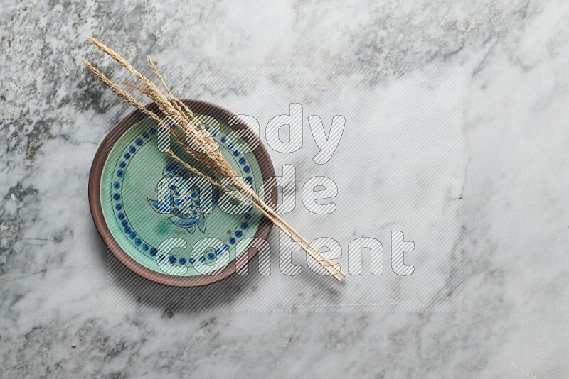 Wheat stalks on decorative pottery plate on grey marble background