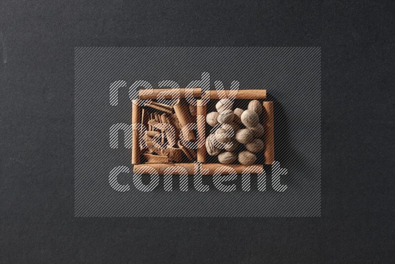 مربعان من أعواد القرفة ممتلئان بقطع من القرفة وجوزة الطيب علي خلفية سوداء