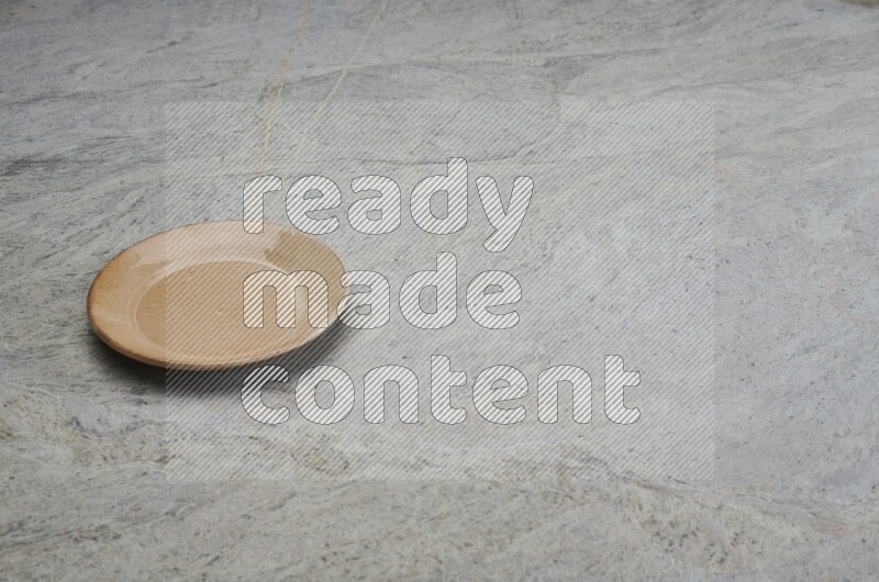 A beige pottery plate on grey marble background