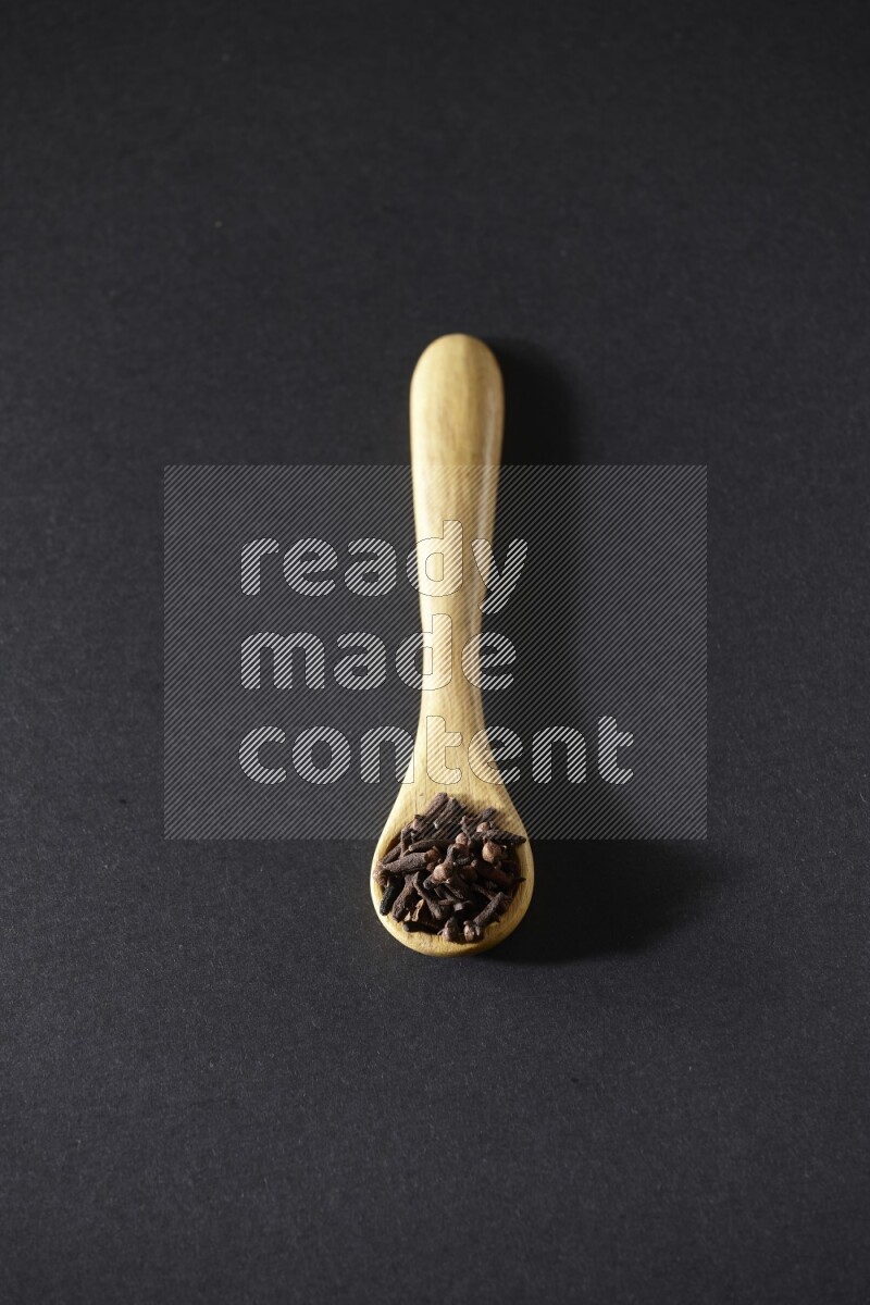 A wooden spoon full of cloves on a black flooring