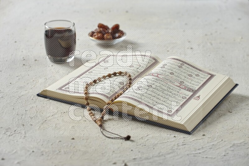 Quran with dates, prayer beads and different drinks all placed on textured white background