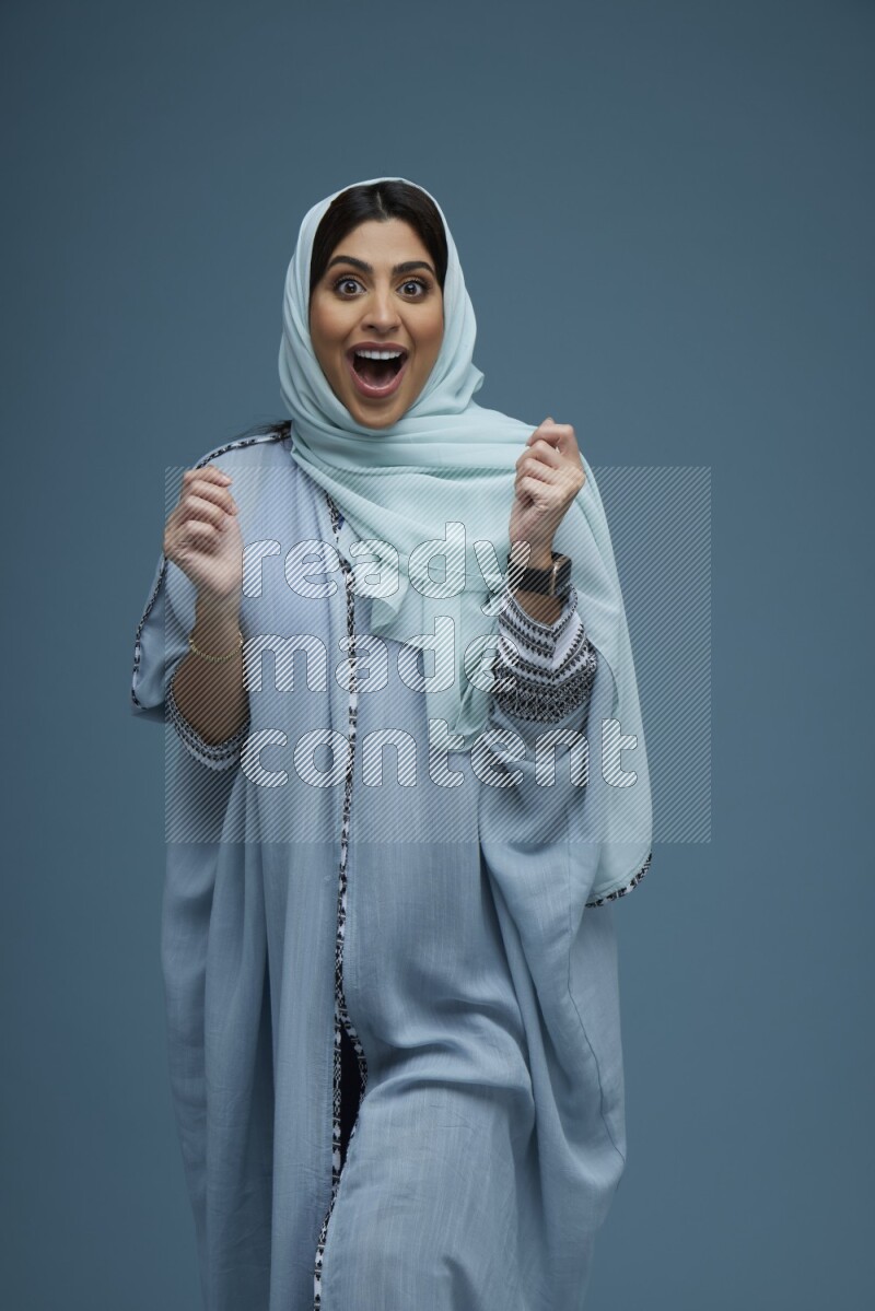 A woman posing in a blue background wearing a blue Abaya with hijab