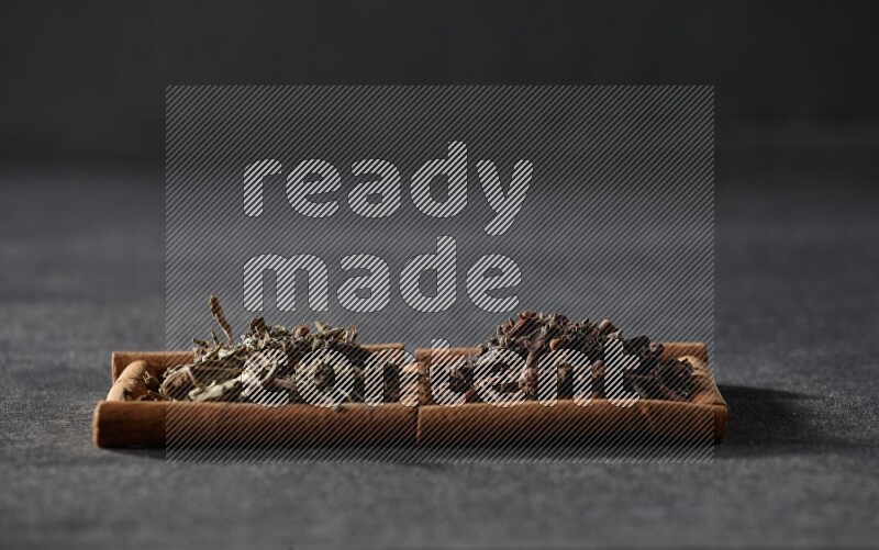 مربعان من أعواد القرفة ممتلئان بالقرنفل والريحان المجفف علي خلفية سوداء