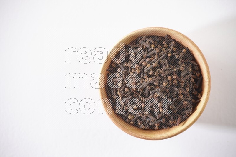 A wooden bowl full of cloves on a white flooring