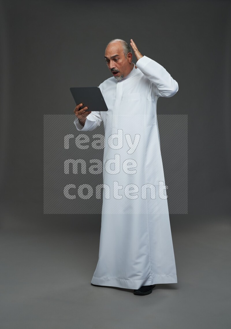 Saudi man without shomag Standing working on tablet on gray background