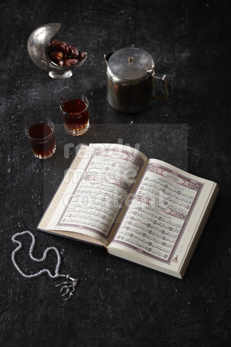Moshaf with tea cups and prayer beads in a dark setup