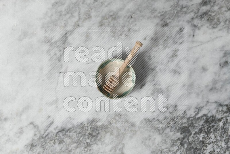 Multicolored pottery bowl with wooden honey dipper in it on grey marble background