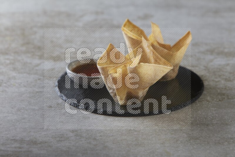 wonton cups with soy sauce ramkin on circle slate on grey textured counter top