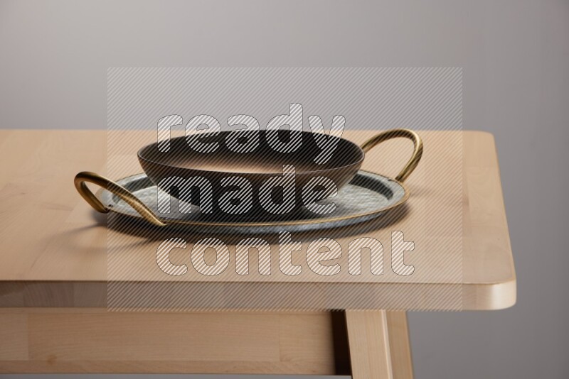 brass plate placed on a rounded stainless steel tray with golden handels on the edge of wooden table
