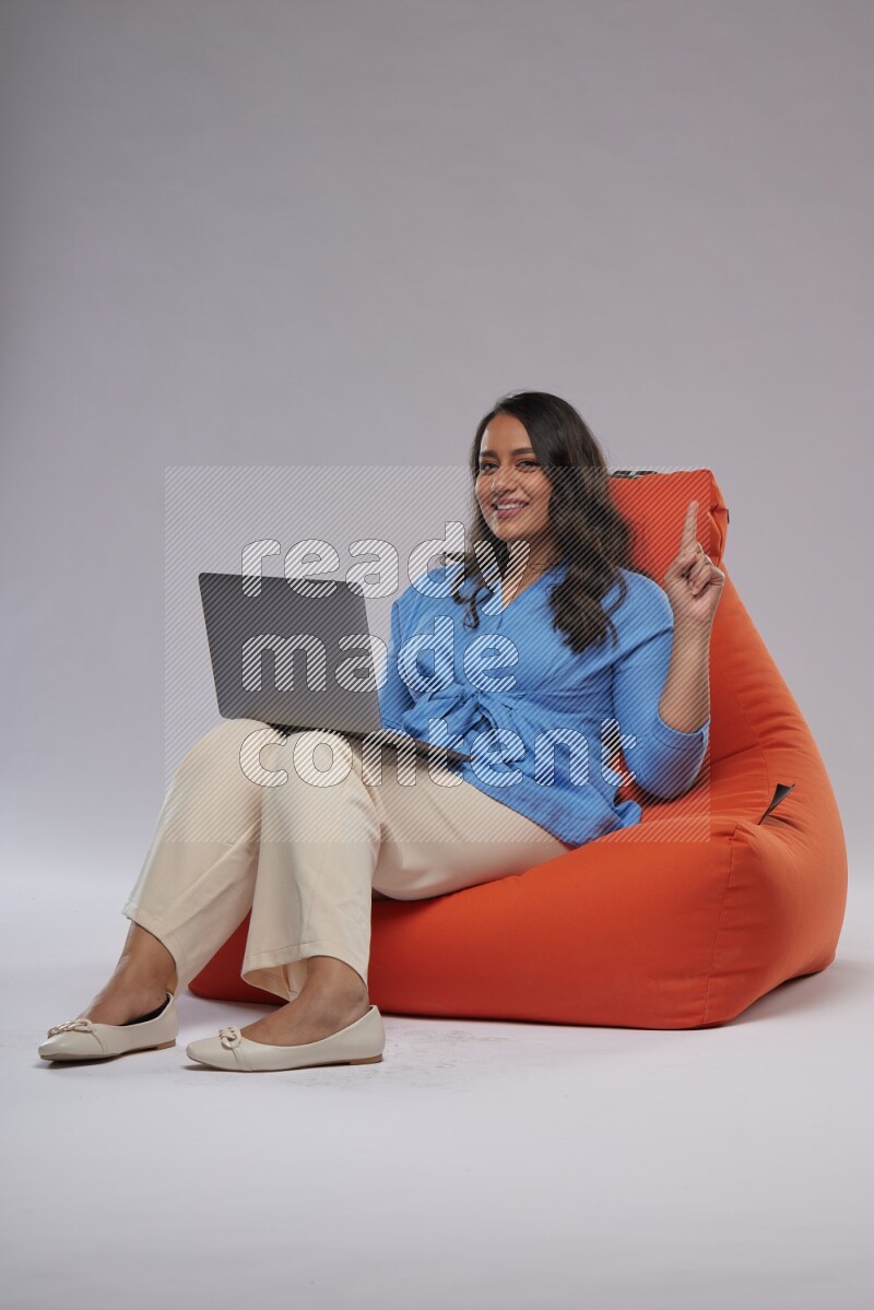 A woman sitting on an orange beanbag and working on laptop