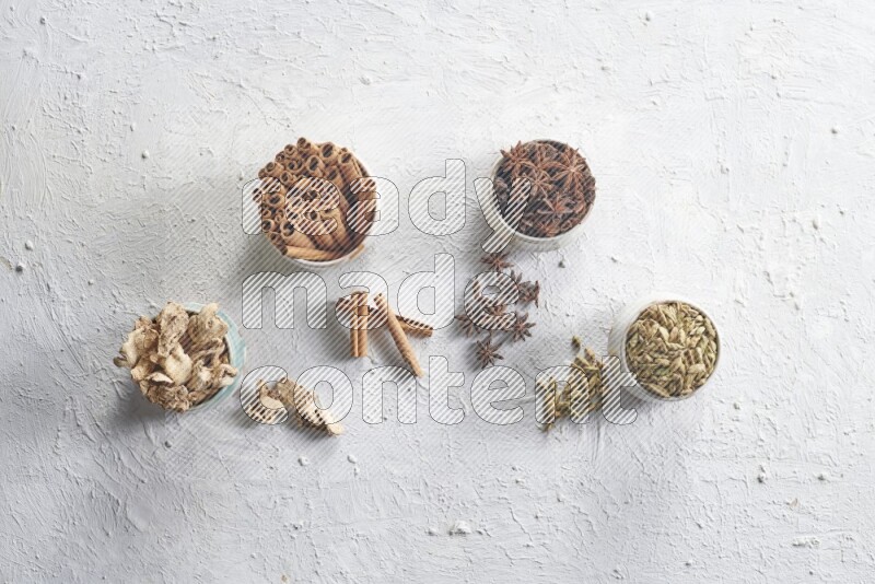 Cardamom, ginger, cinnamon sticks and star anise in 4 bowls on a textured white background
