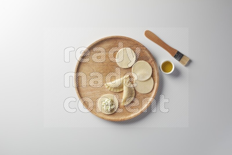two closed sambosas and one open sambosa filled with cheese while oil with oil brush aside in a wooden dish on a white background