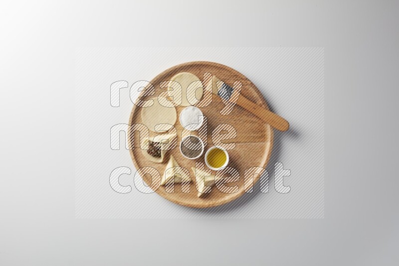 two closed sambosas and one open sambosa filled with meat while salt, black pepper and oil with oil brush aside in a wooden dish on a white background