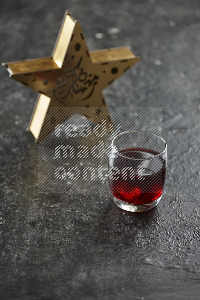 A wooden golden star lantern with different drinks, dates, nuts, prayer beads and quran on textured black background