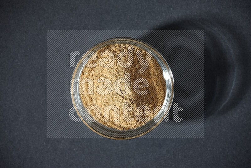 A glass bowl full of cumin powder on black flooring