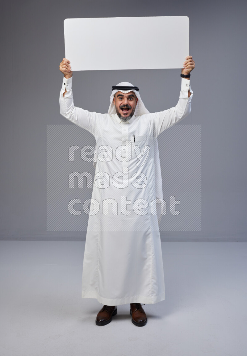 Saudi man Wearing Thob and white Shomag standing holding board on Gray background