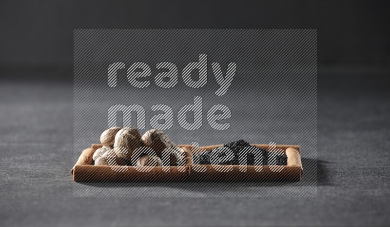 2 squares of cinnamon sticks full of black seeds and nutmeg on black flooring