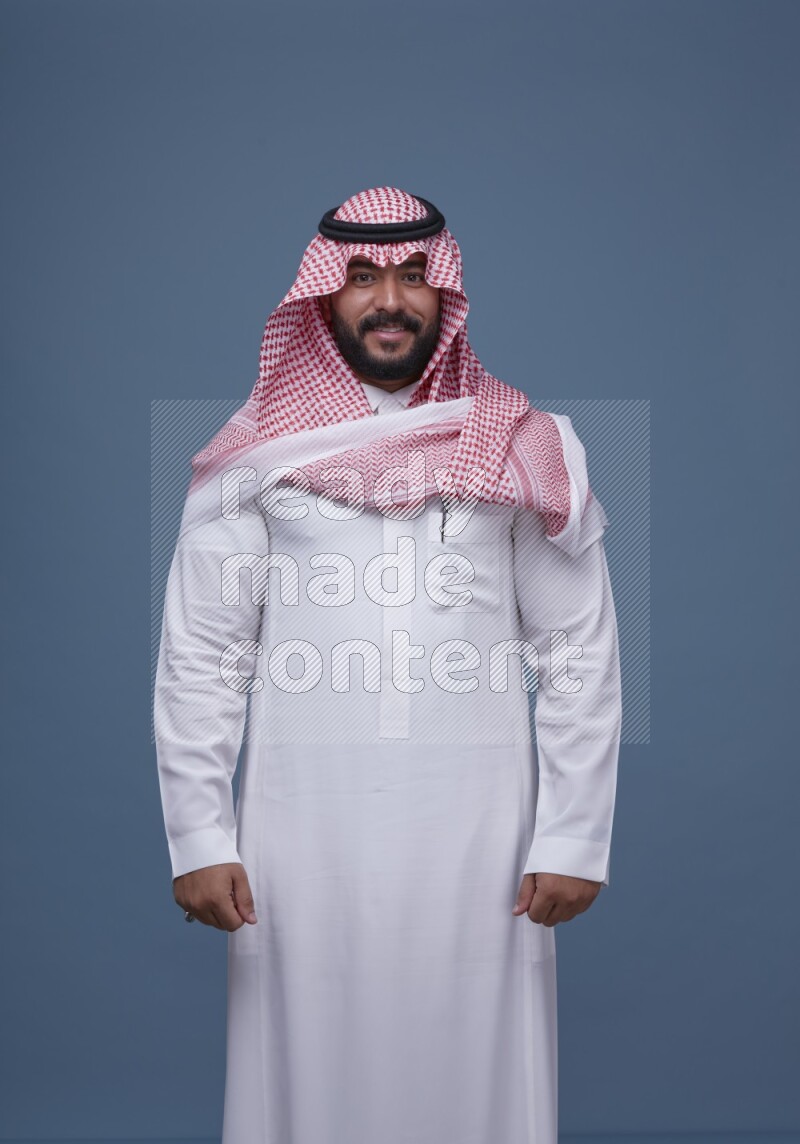 A Saudi man posing on blue background wearing Thob and Shomag