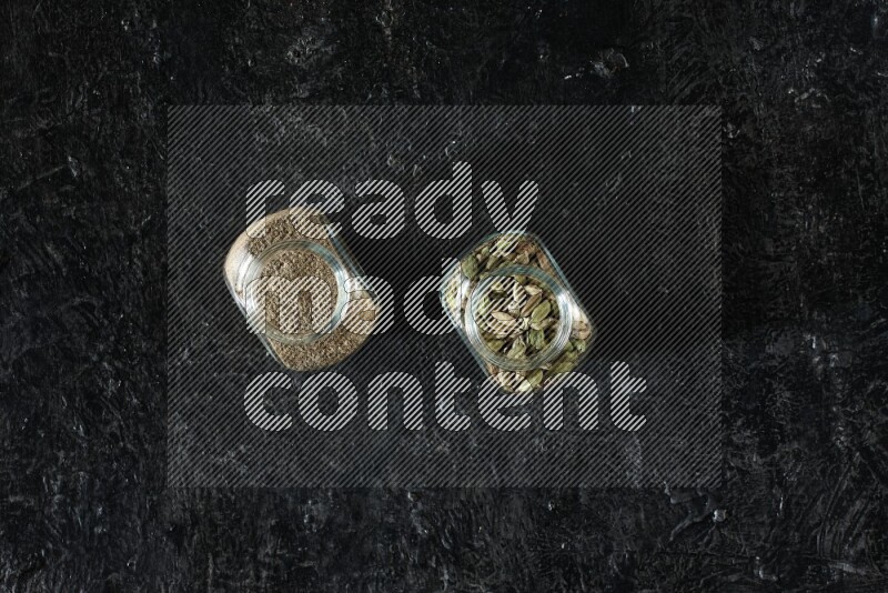 وعاءان زجاجيان ممتلئان ببودرة الهيل وحبوب الهيل على خلفية سوداء