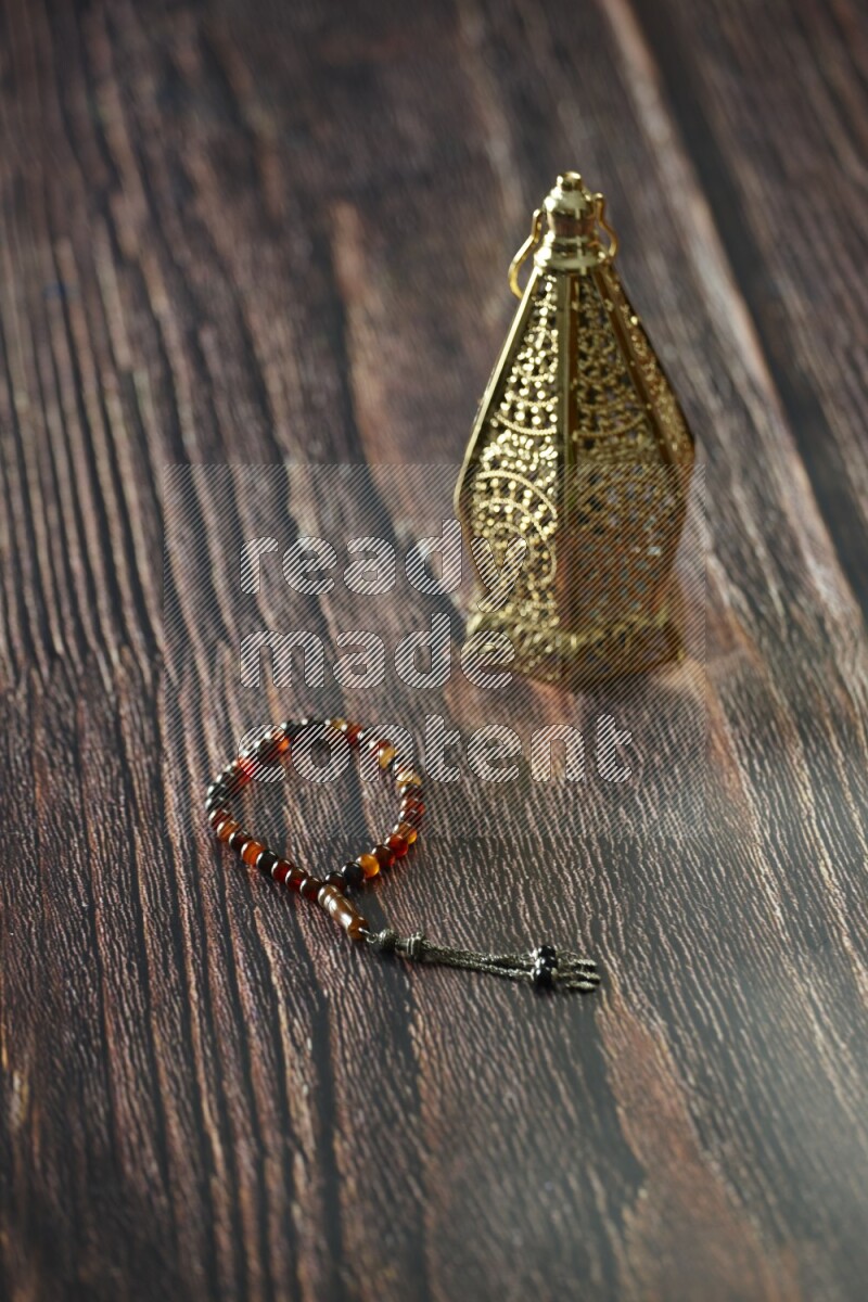 A golden lantern with different drinks, dates, nuts, prayer beads and quran on brown wooden background