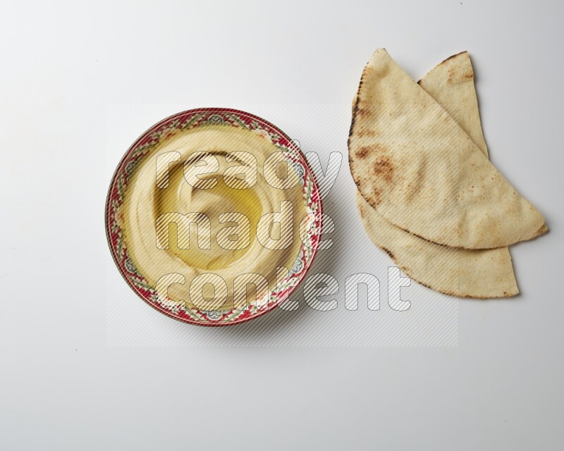 Hummus in a red plate with patterns garnished with olive oil on a white background