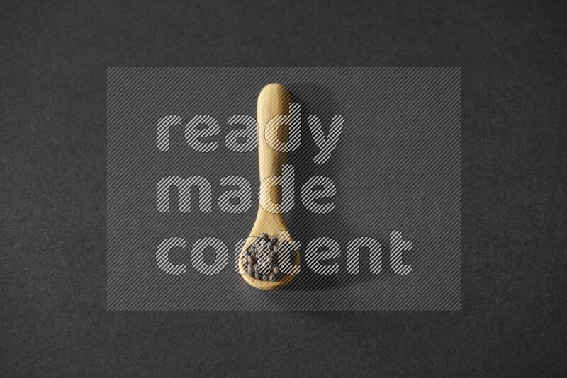 A wooden spoon full of black pepper on a black flooring