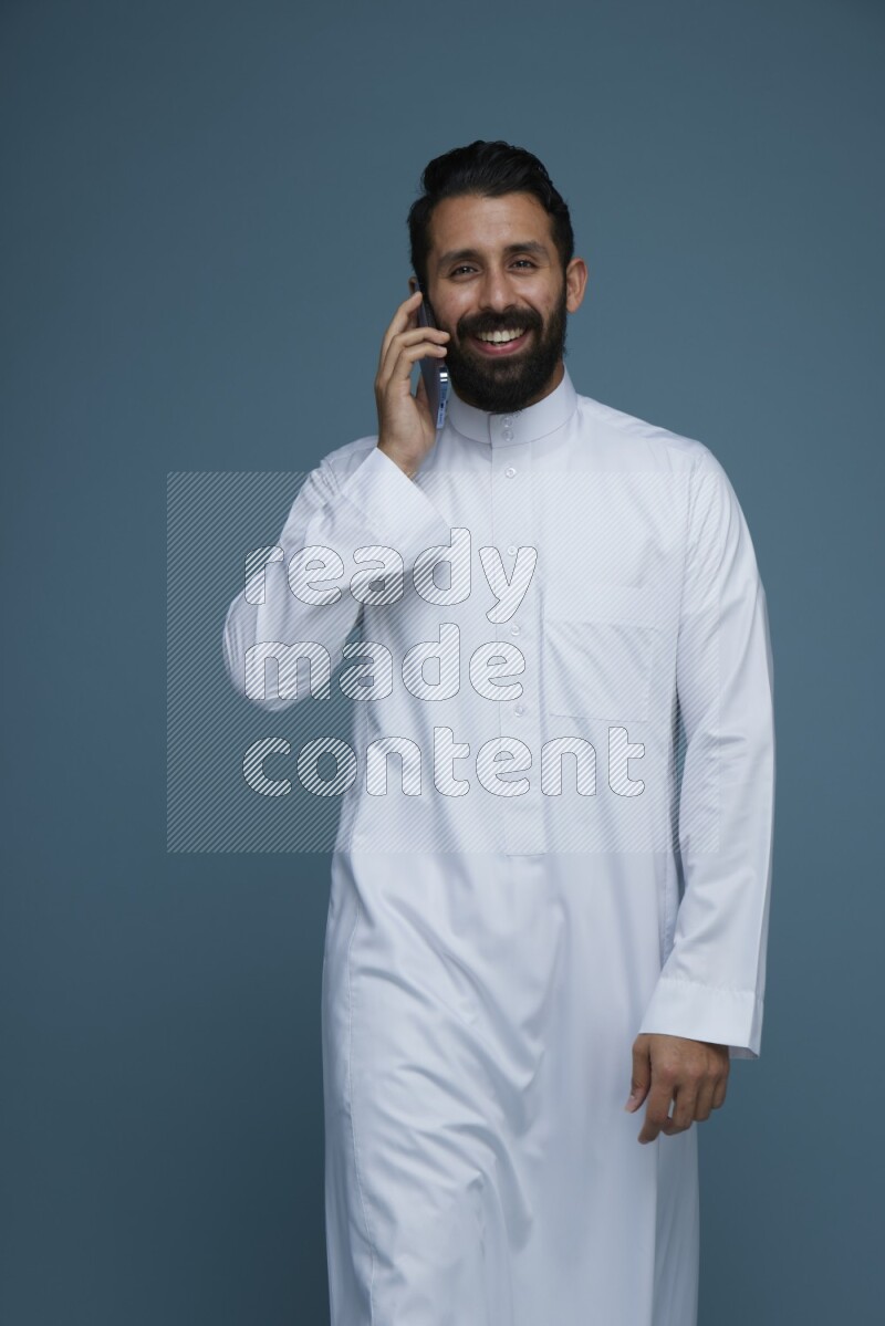 A man having a call on a blue background wearing Saudi Thob