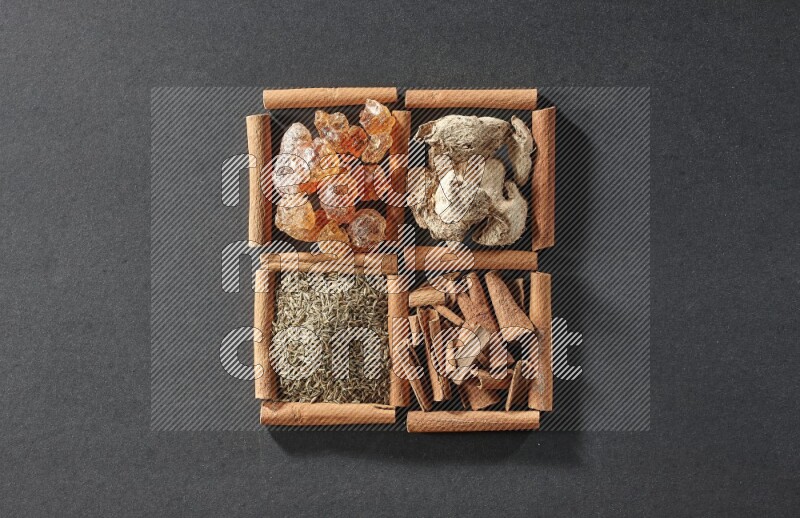 4 مربعات من عيدان القرفة ممتلئة بالصمغ العربي والزنجبيل المجفف وقطع القرفة والكمون على أرضية سوداء