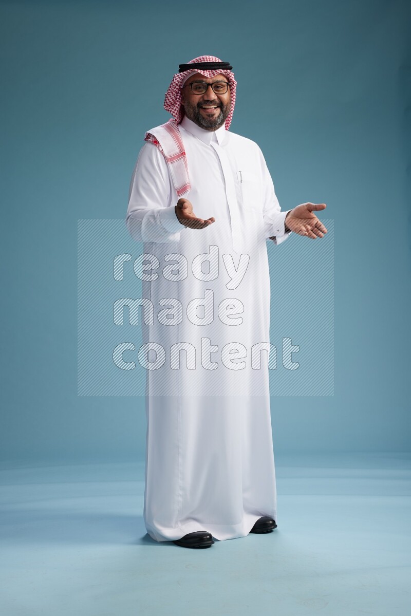Saudi Man with shimag Standing Interacting with the camera on blue background