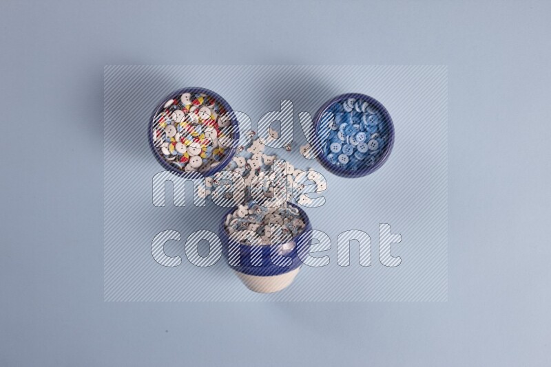Multicolored pottery bowls full of colored buttons on blue background