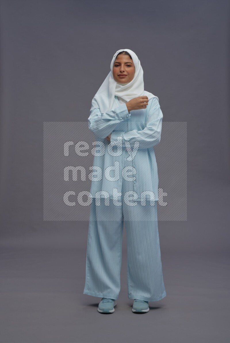 Saudi woman wearing hijab clothes standing with crossed arms on gray background