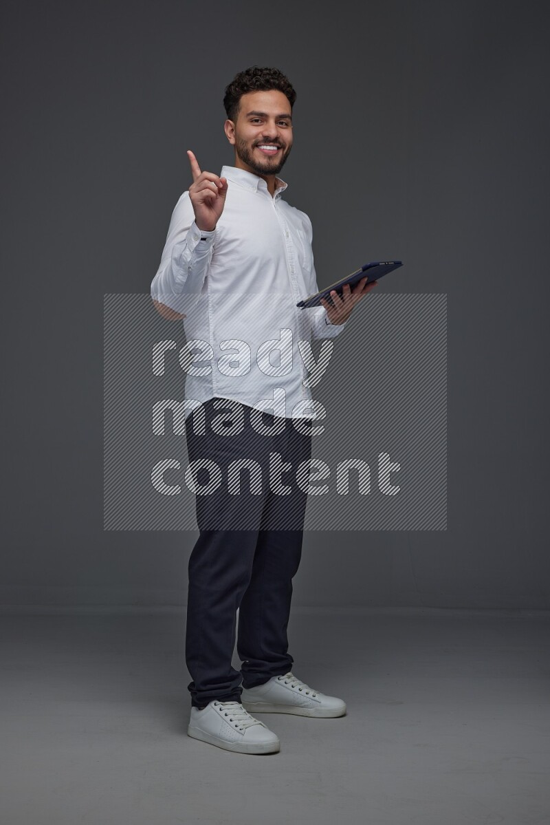 A man wearing smart casual standing and using his tablet and making multi hand gestures eye level on a gray background