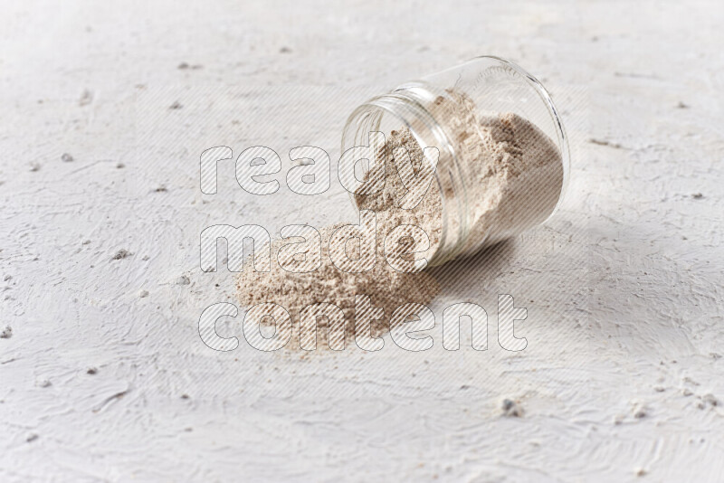 A glass jar full of onion powder flipped with some spilling powder on white background