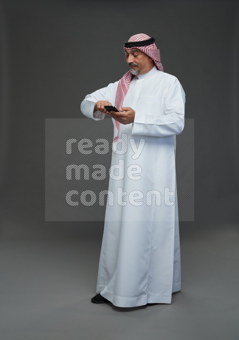 Saudi man with shomag Standing texting on phone on gray background