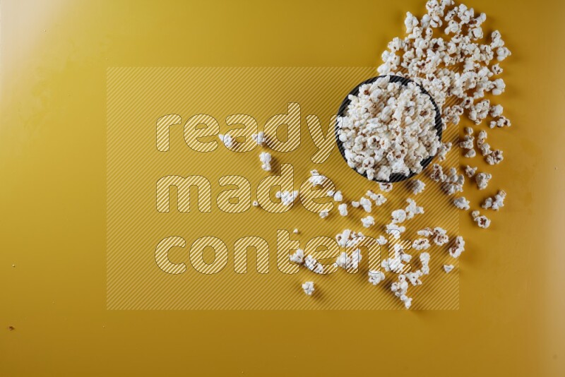 A black ceramic bowl full of popcorn with popcorn beside it on a yellow background in different angles
