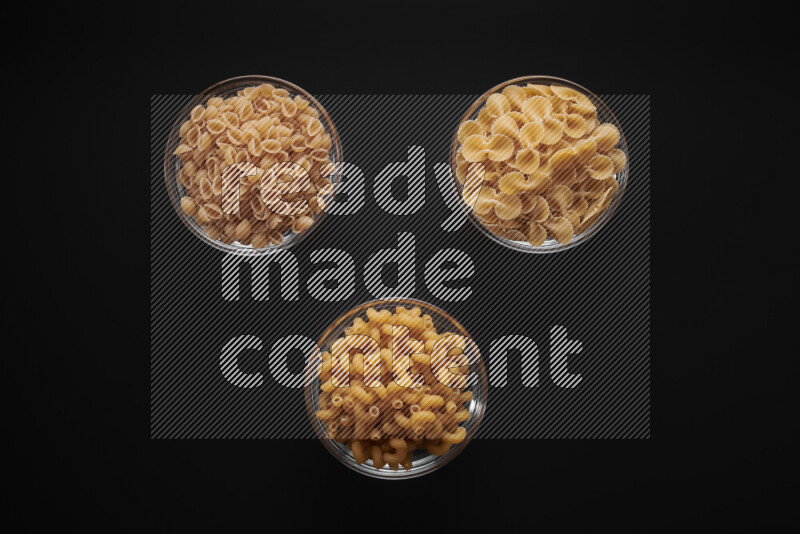Different pasta types in glass bowls on black background