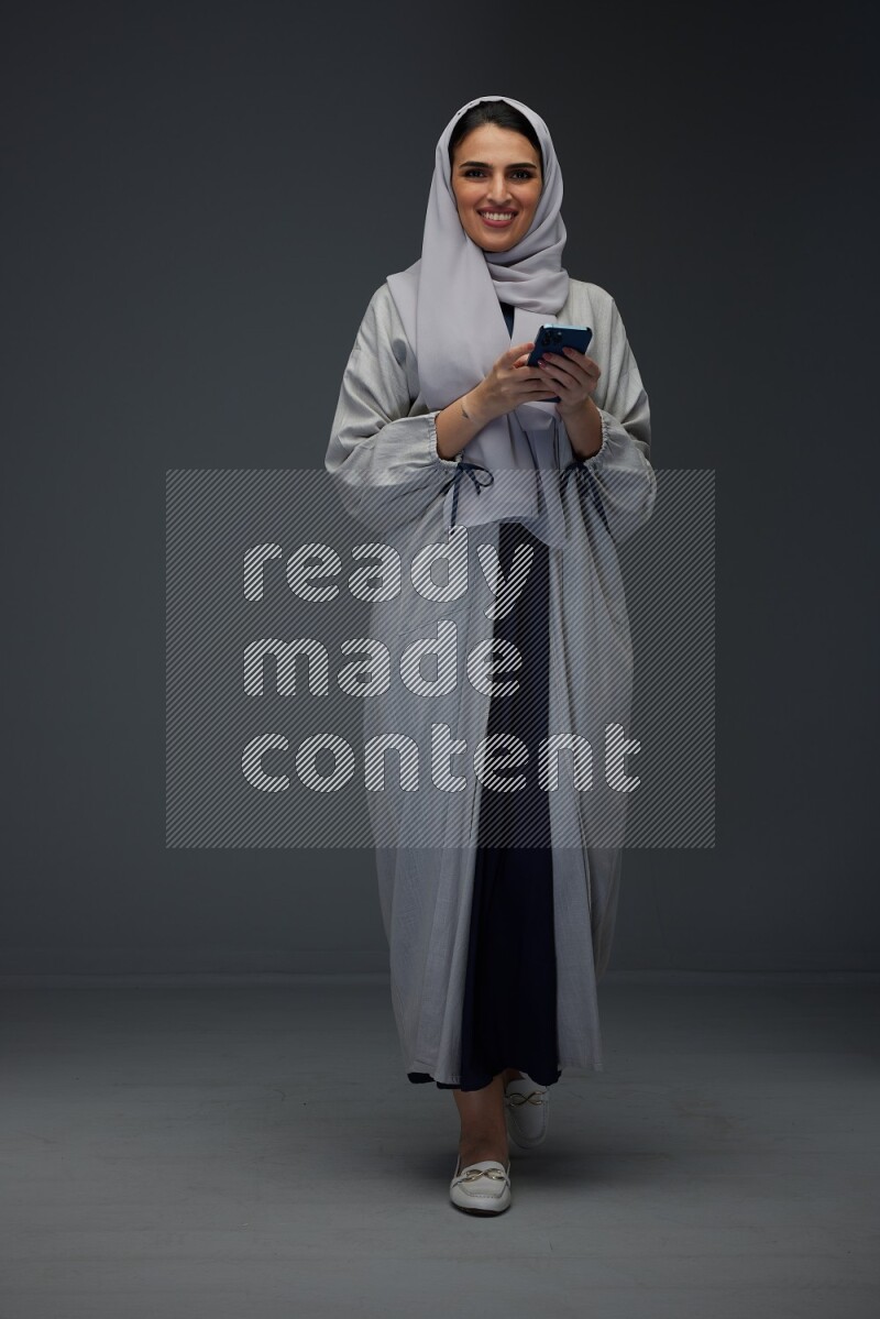 A Saudi woman Texting wearing Grey Abaya on a grey background