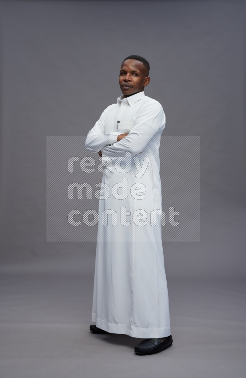 Saudi man wearing thob standing with crossed arms on gray background