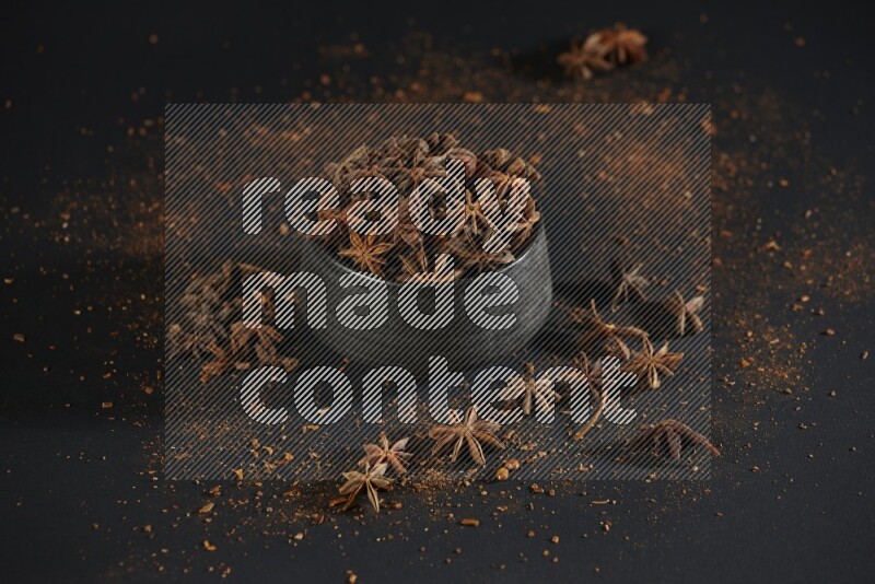 Star Anise in a black bowl with sprinkled anise on black flooring