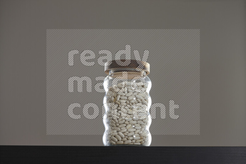 White beans in a glass jar on black background