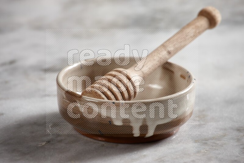 Multicolored pottery bowl with wooden honey dipper in it on grey marble background