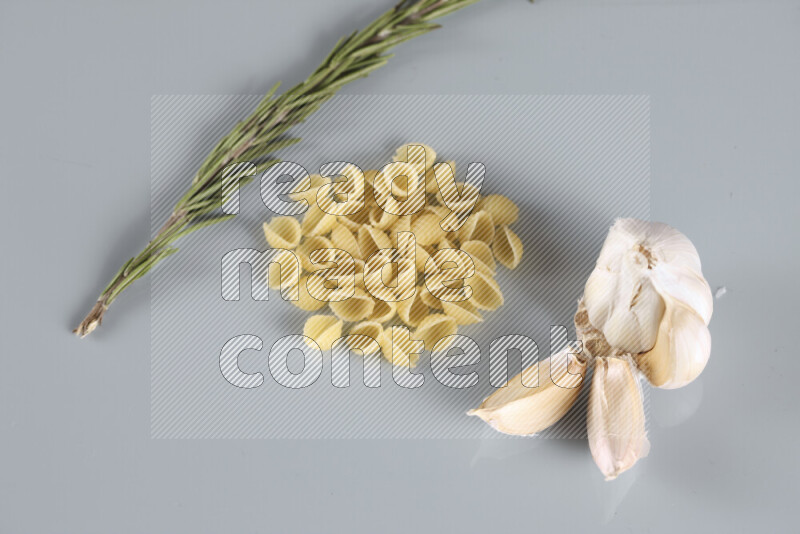 Raw pasta with different ingredients such as cherry tomatoes, garlic, onions, red chilis, black pepper, white pepper, bay laurel leaves, rosemary, cardamom and mushrooms on light blue background