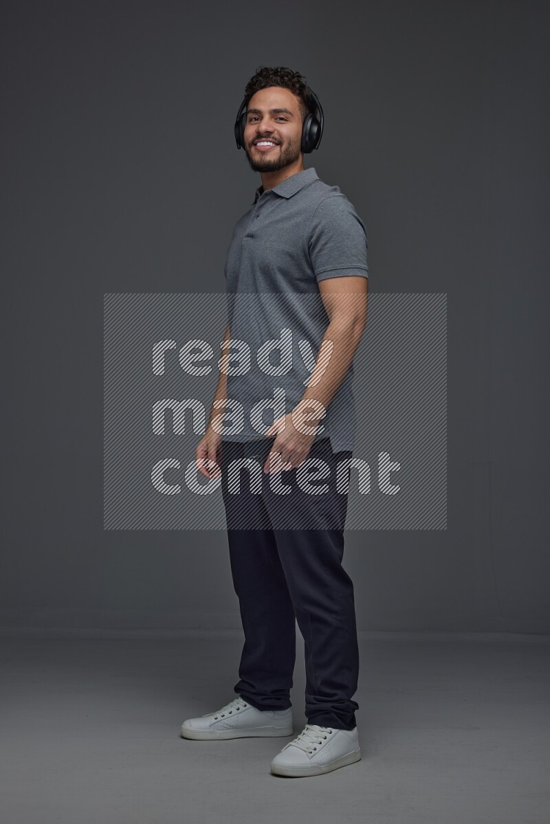 A man wearing casual and using his phone and headphone eye level on a gray background