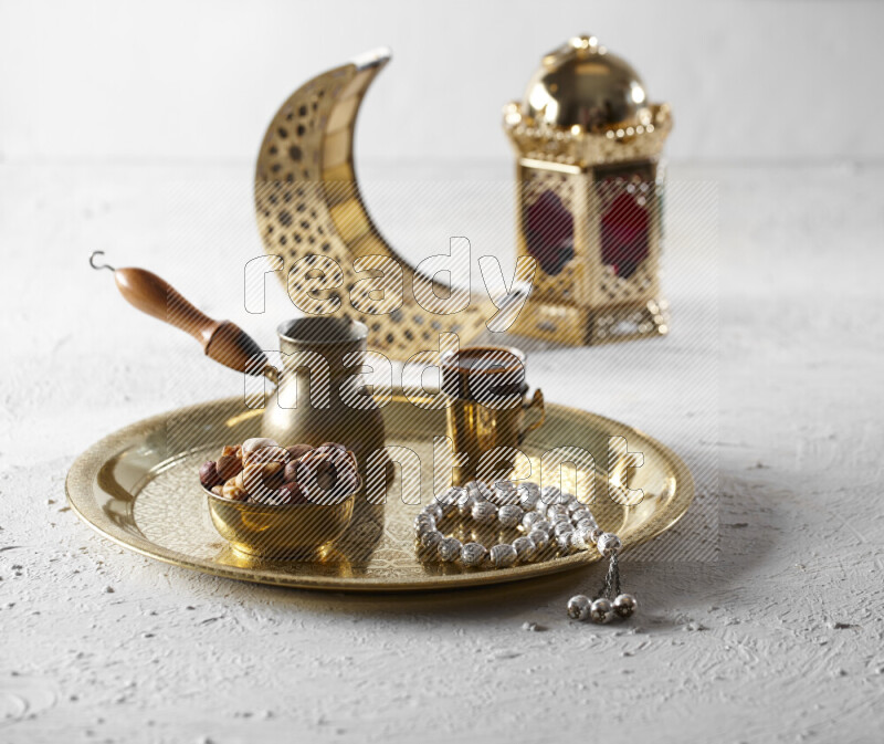 Nuts in a metal bowl with coffee and prayer beads on a tray beside lanterns in a light setup