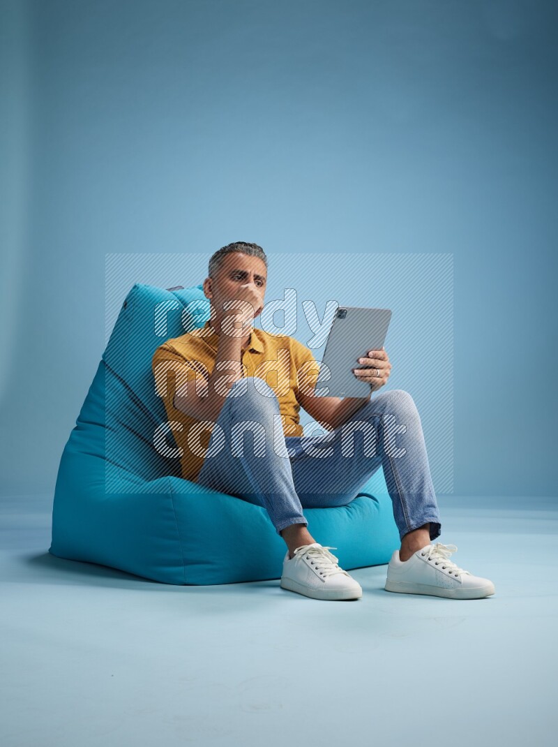 A man sitting on a blue beanbag and working on tablet