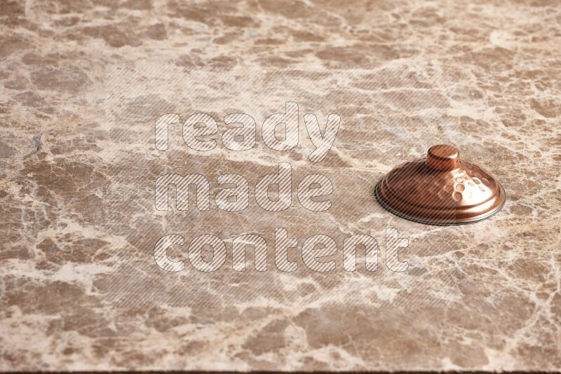 A small copper pot lid on beige marble background