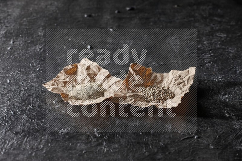 White pepper beads and powder in 2 crumpled paper on textured black flooring